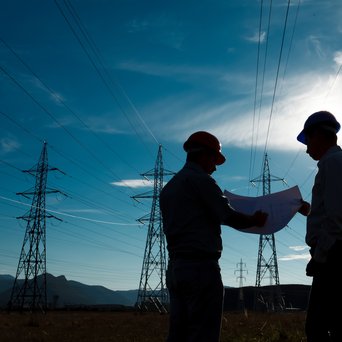 silhouette-of-two-engineers-standing-at-electricity-station-discussing-plan-222500491